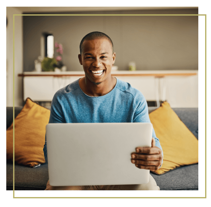 man on a couch holding a laptop computer and smiling.